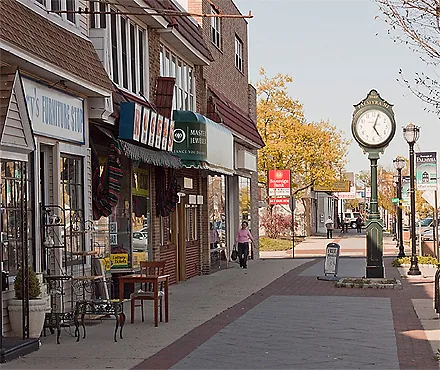 Historic downtown street with brick storefronts, sidewalk clock, and autumn trees